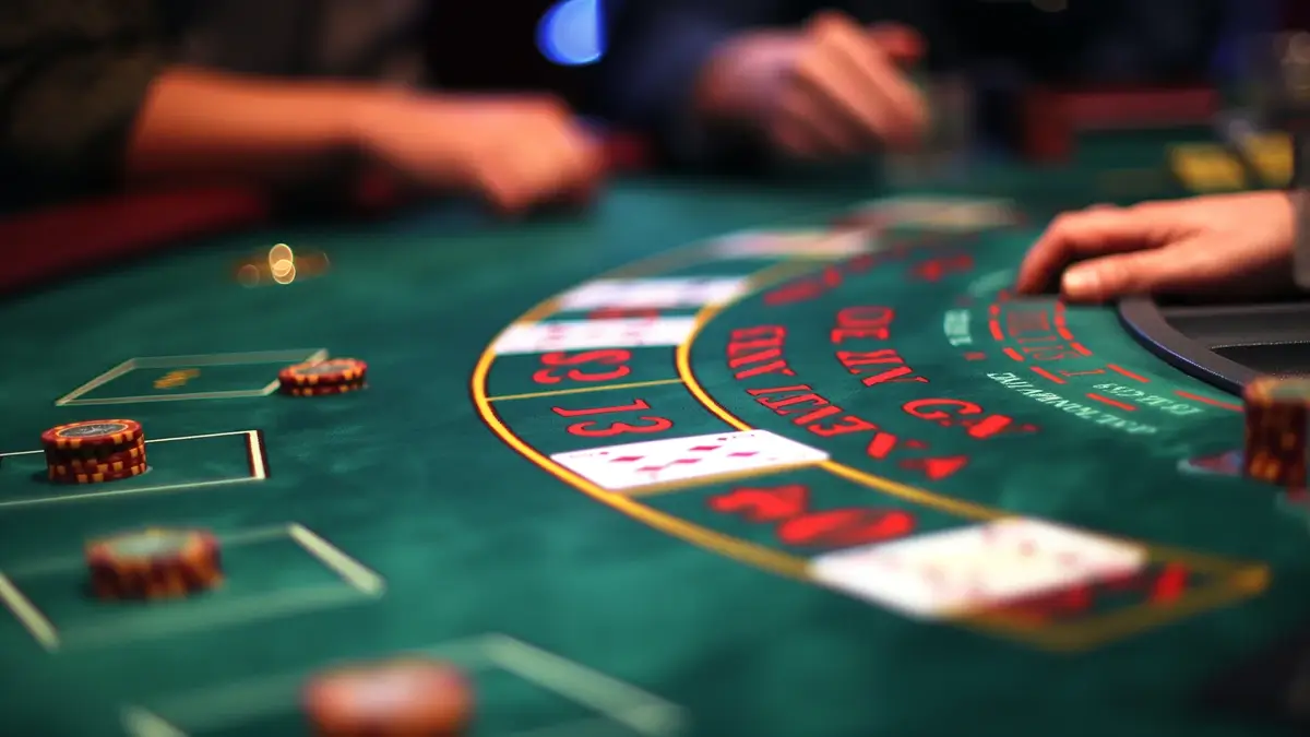 A close-up view of a blackjack table with several chips and cards laid out. The focus is on the table's layout, showing different betting areas and some players' hands.